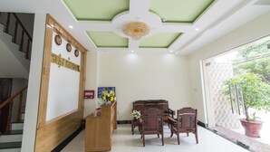 A reception area with a wooden desk, a chandelier, a staircase, and a potted plant.