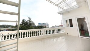 A spacious balcony with a white railing and a glass ceiling, overlooking a cityscape with buildings and trees.