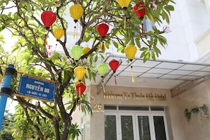 L’entrée d’un immeuble, avec une enseigne indiquant « Bienvenue à l’hôtel Thanh Hien » et un panneau de rue indiquant « Nguyen Du » et « Loi Giang 12 (M) ».