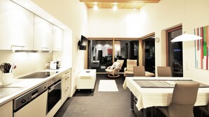 Una cocina compacta con electrodomésticos modernos, una zona de comedor con mesa y sillas, y vistas a un espacio de estar a través de un vidrio.