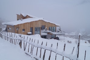 A wooden house with a balcony, surrounded by a snow-covered fence.