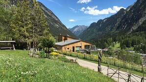 Una casa moderna de madera con techo inclinado, rodeada de abundante vegetación y montañas al fondo.