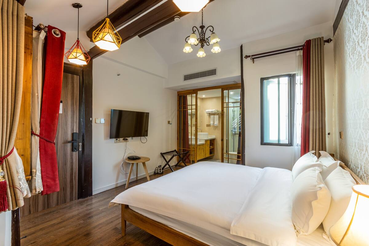 Een hotelkamer met een groot bed, een televisie, een houten vloer en een raam met gordijnen.