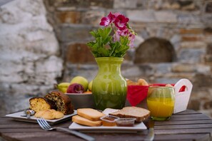A breakfast setting with bread, pastries, a glass of orange juice, a vase with flowers, and a fruit bowl. - Villa Thimianos (Naxos)