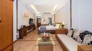 Een moderne hotelkamer met een glazen bijzettafeltje, een bank, een bed, een televisie en een badkamer in de achtergrond.