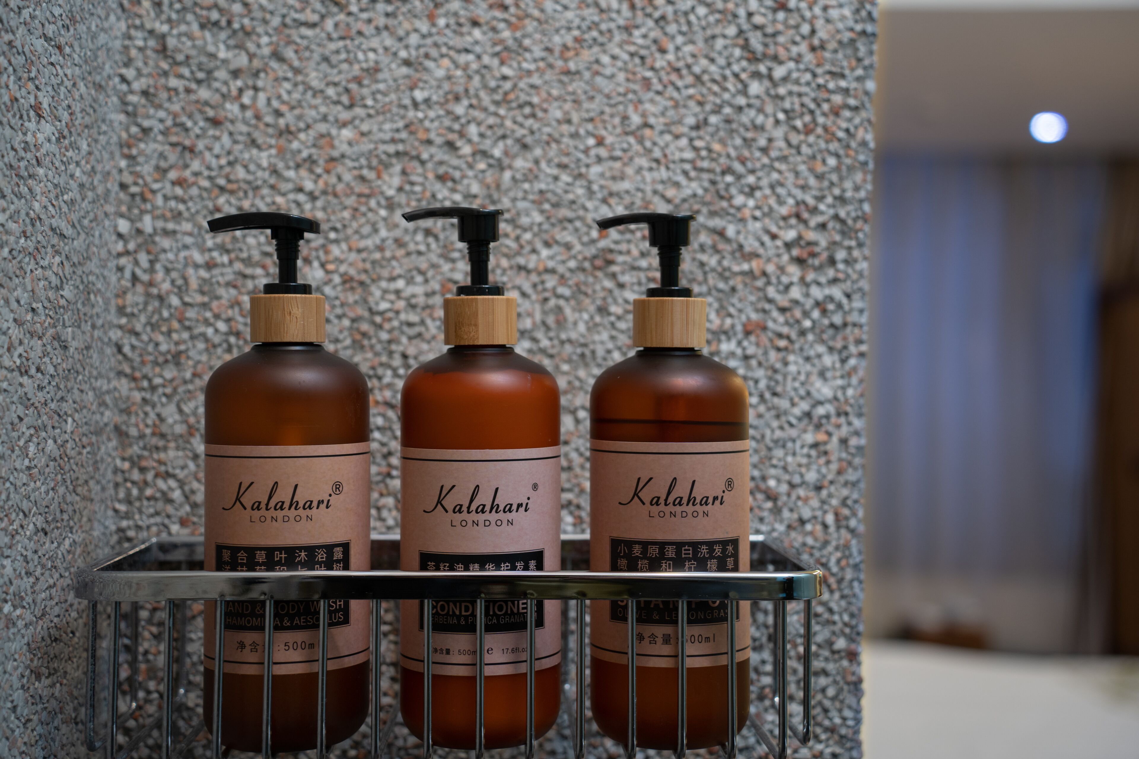 Three bottles of Kalahari London soap on a metal shelf against a speckled wall.
