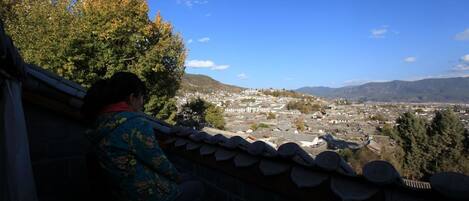 A person sitting on a balcony overlooking a cityscape with mountains in the background.
