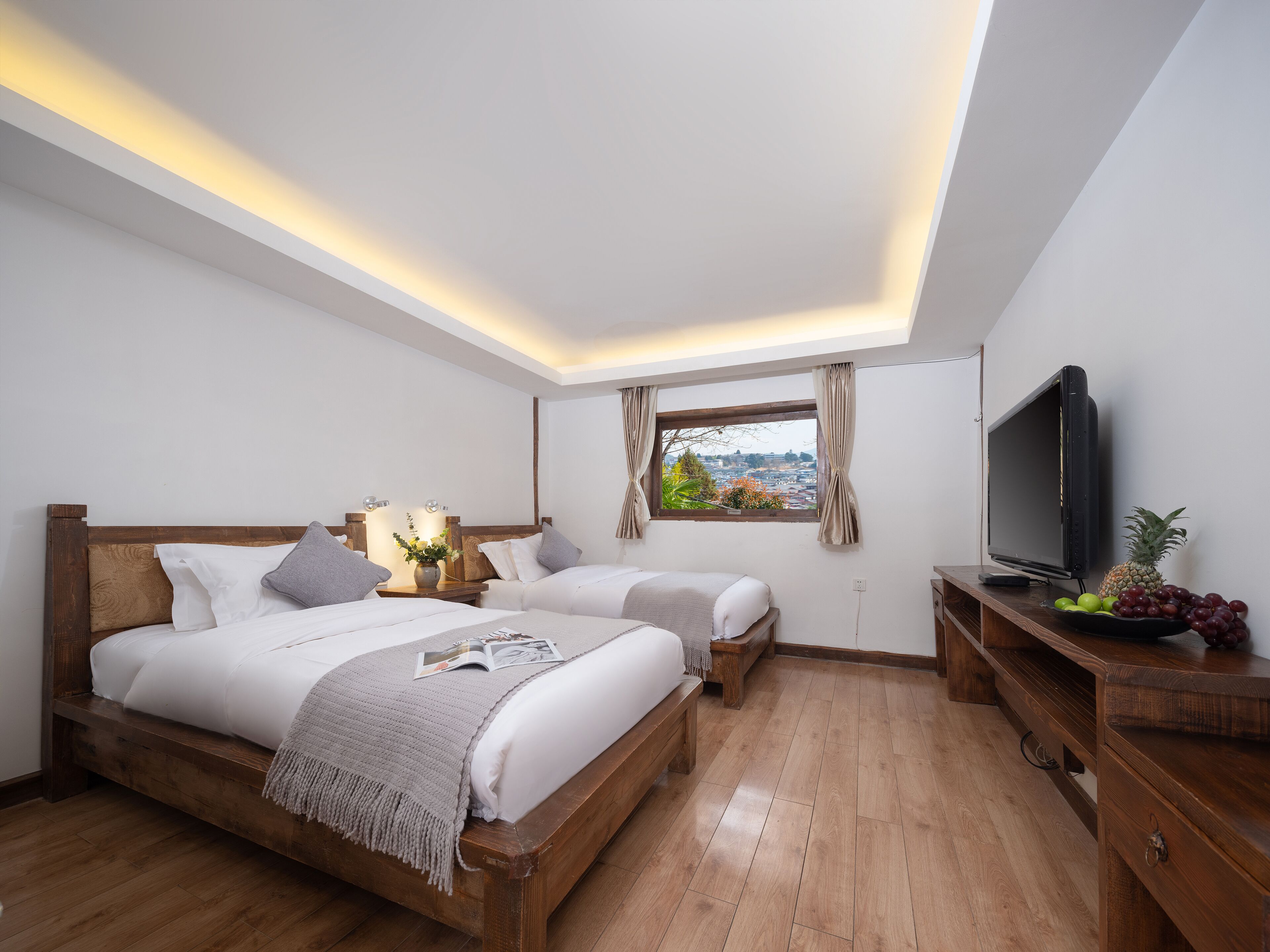 A hotel room with two beds, a television, a window with a view, and a fruit bowl.
