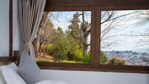Een slaapkamer met een groot raam, een bed en uitzicht op bomen en een stadsbeeld.