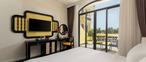 A hotel room with a large bed, a desk with a flat-screen TV, a mirror, and a view of the outdoor terrace.