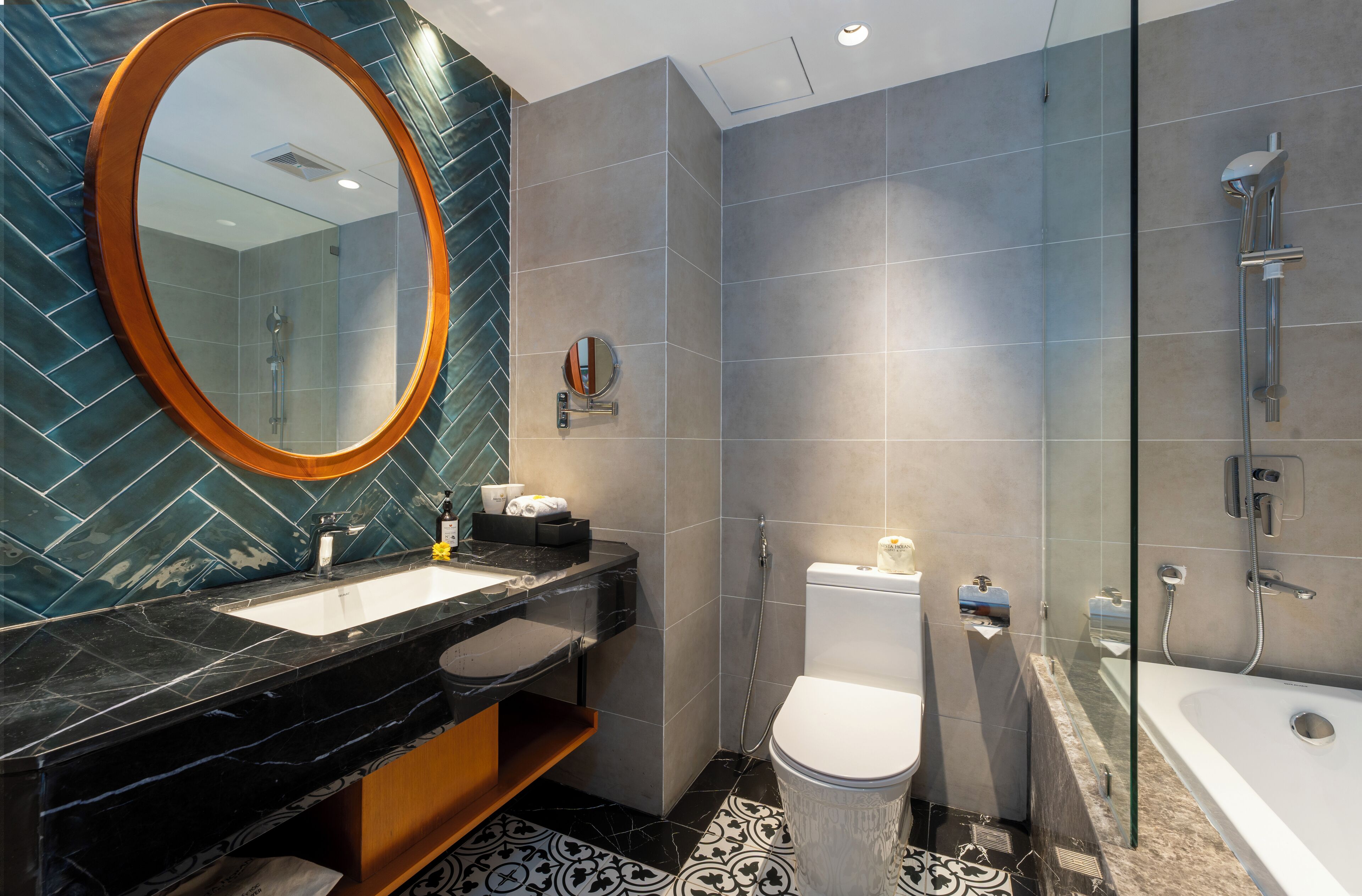 Et moderne badeværelse med en sort marmorvask, et rundt spejl, et toilet og en brusekabine med glasvægge.