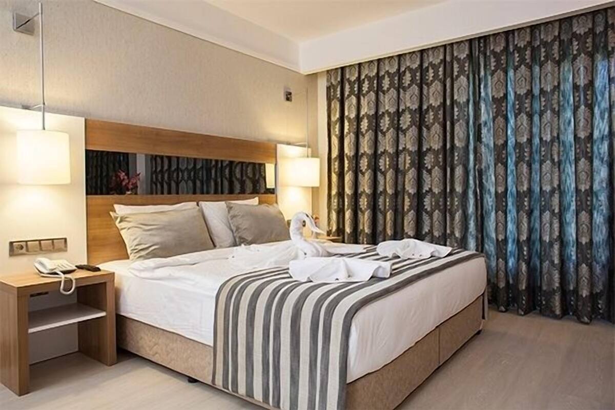 A hotel room with a large bed, bedside lamps, a telephone, and a curtain with a leaf pattern.