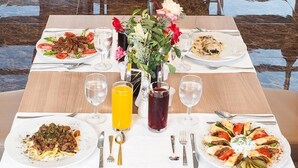 Une table à manger avec quatre assiettes de nourriture, un vase rempli de fleurs et divers verres contenant des boissons.