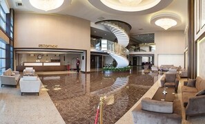 Un hall d’entrée spacieux avec un comptoir d’accueil, un escalier en courbe et des espaces aménagés pour s’asseoir.