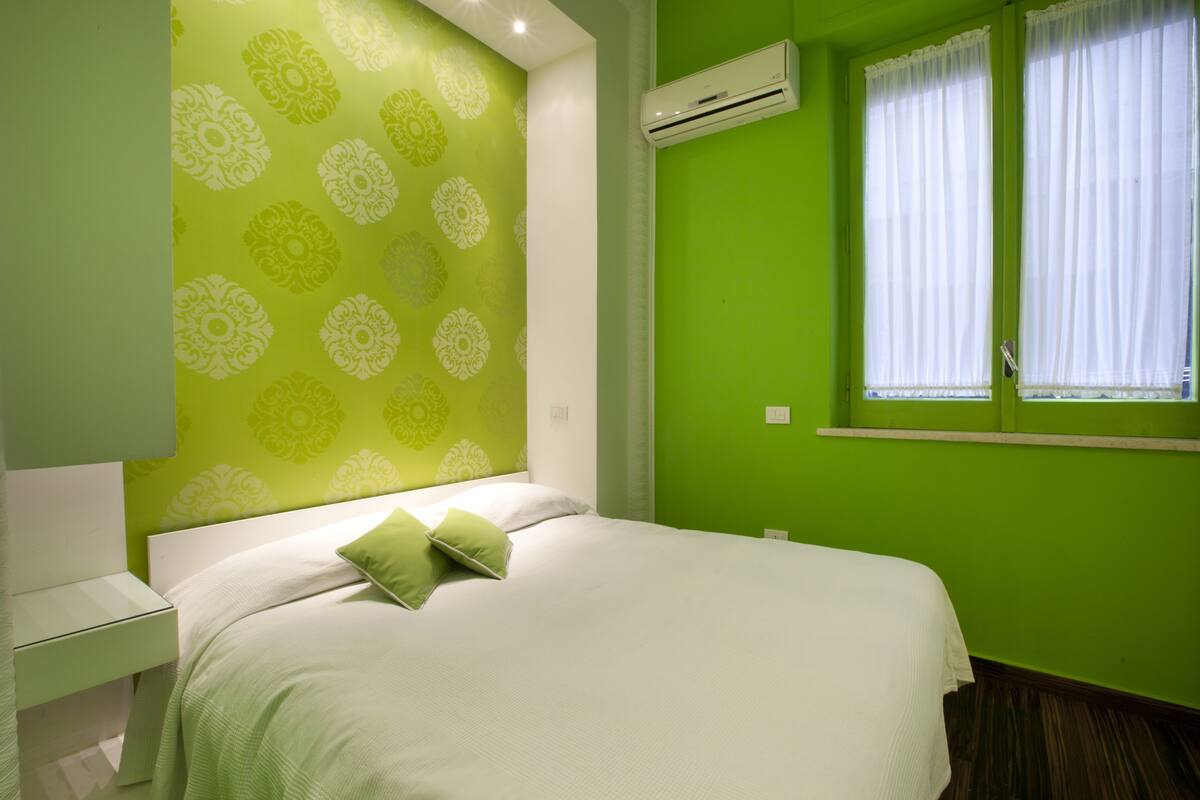 A room with a bed, a nightstand, a window with curtains, and an air conditioning unit.