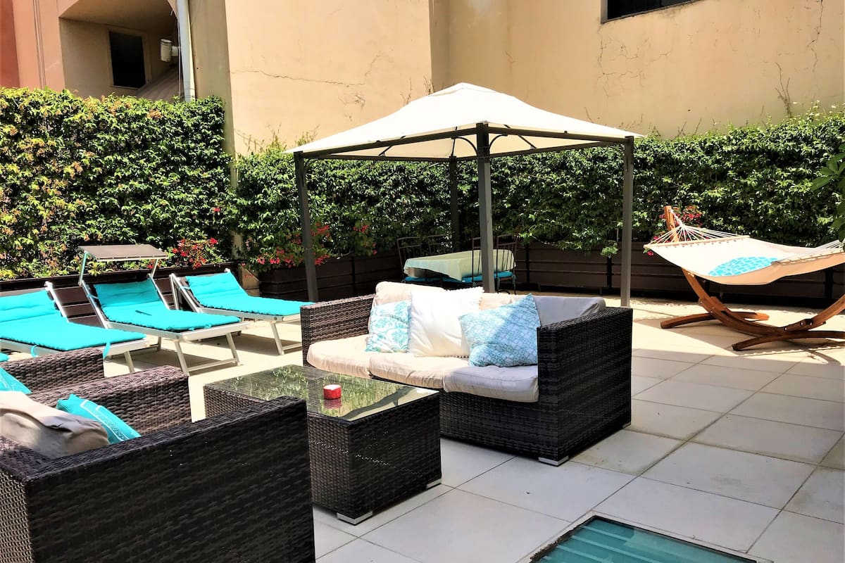 An outdoor patio area with wicker furniture, a glass table, and a hammock.