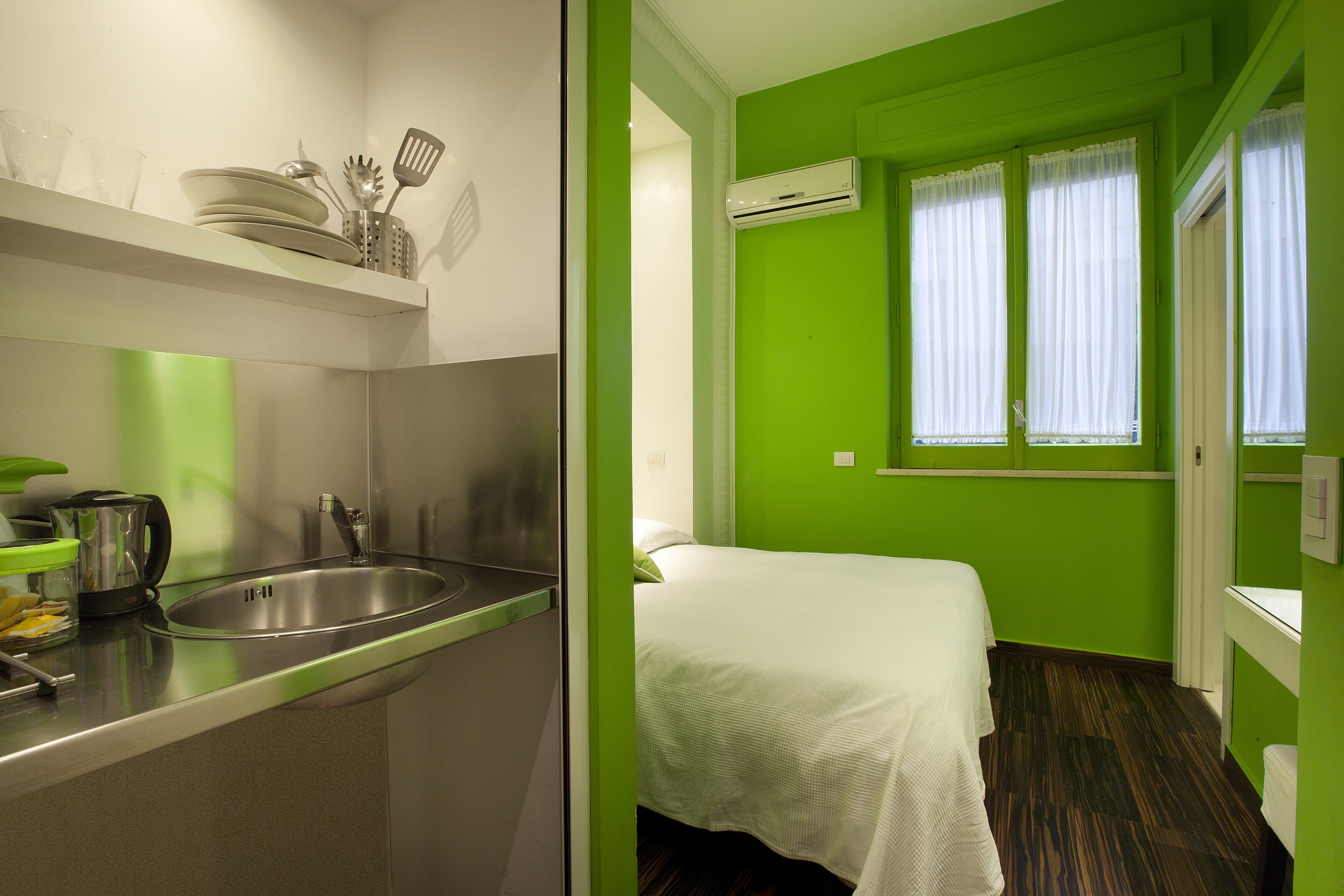 Una habitación de hotel compacta con kitchenette, una cama y una ventana con cortinas.