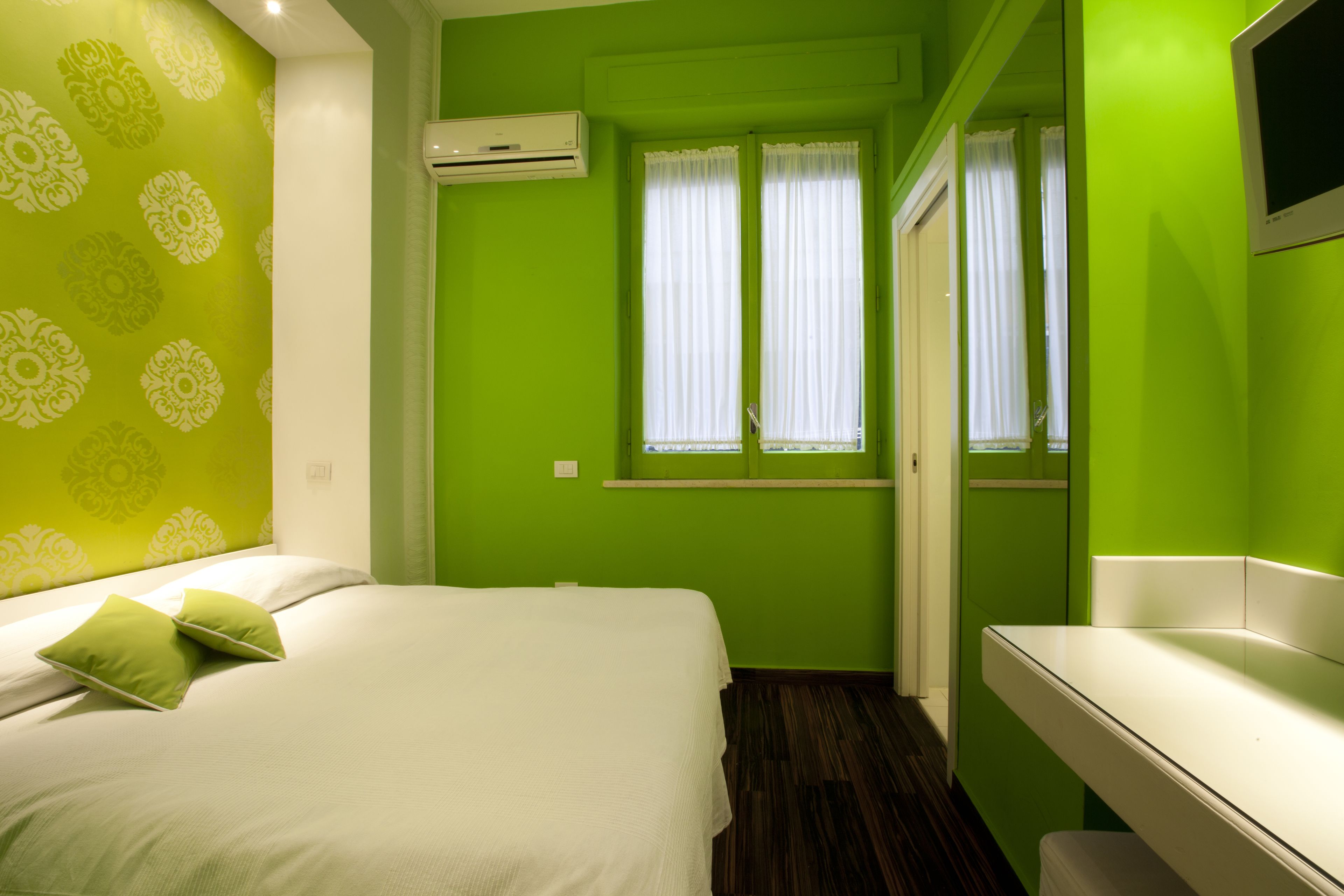 Una habitación con una cama, una mesita de noche blanca, un espejo y una ventana con cortinas.