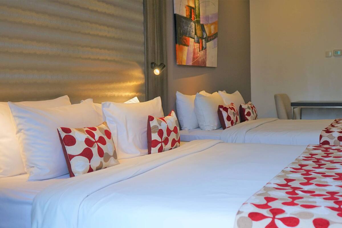Une chambre d’hôtel avec deux lits, du linge de lit blanc et des oreillers à motifs rouges et blancs.