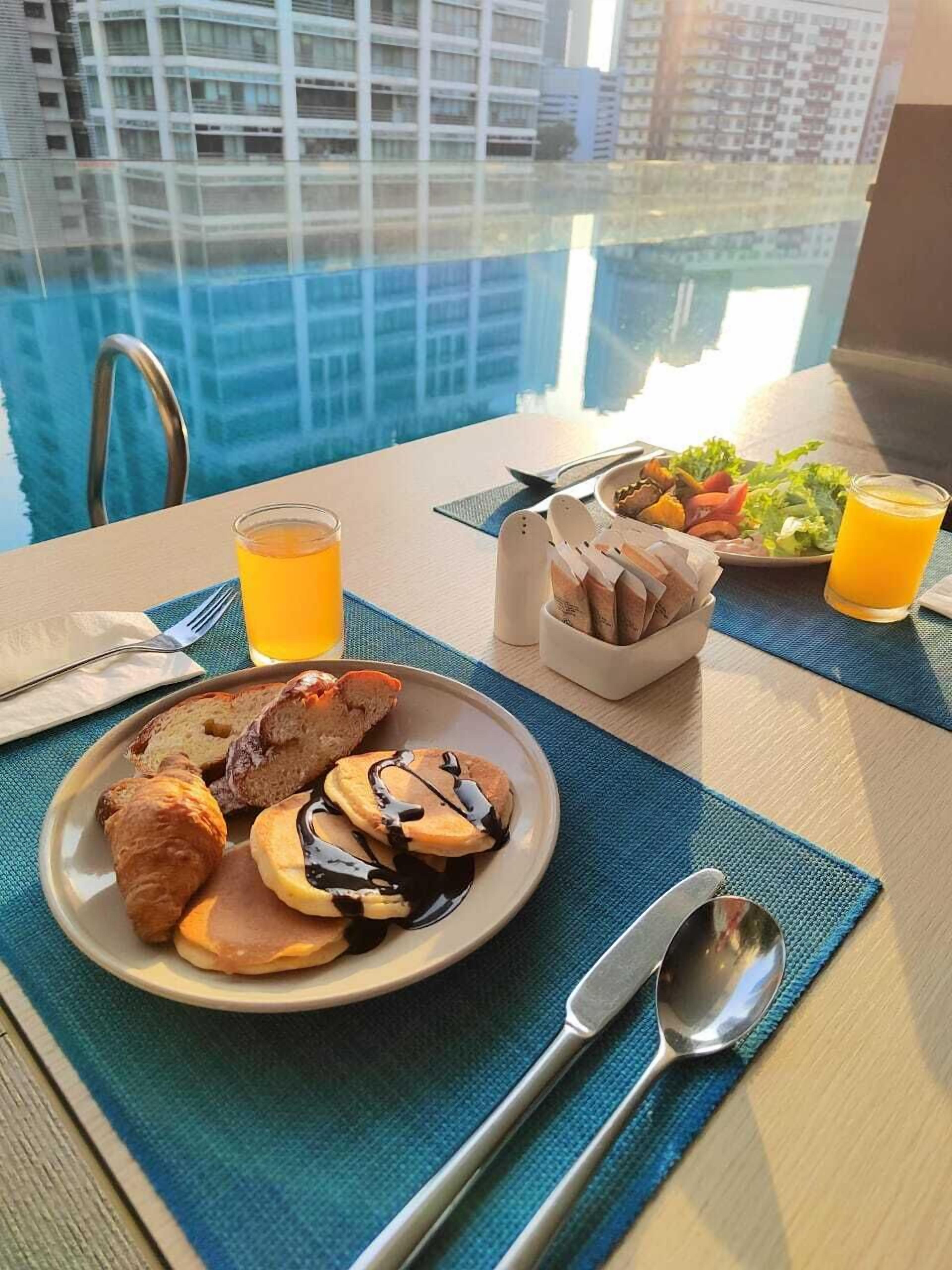 A breakfast setting with croissants, pancakes, and a salad on a table by a pool.