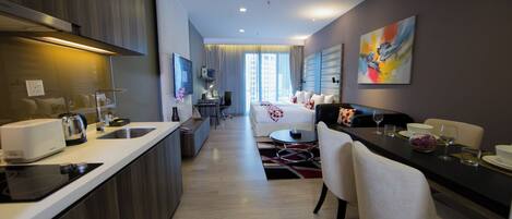 A modern hotel room with a kitchenette, a dining area, a bed, and a large window.