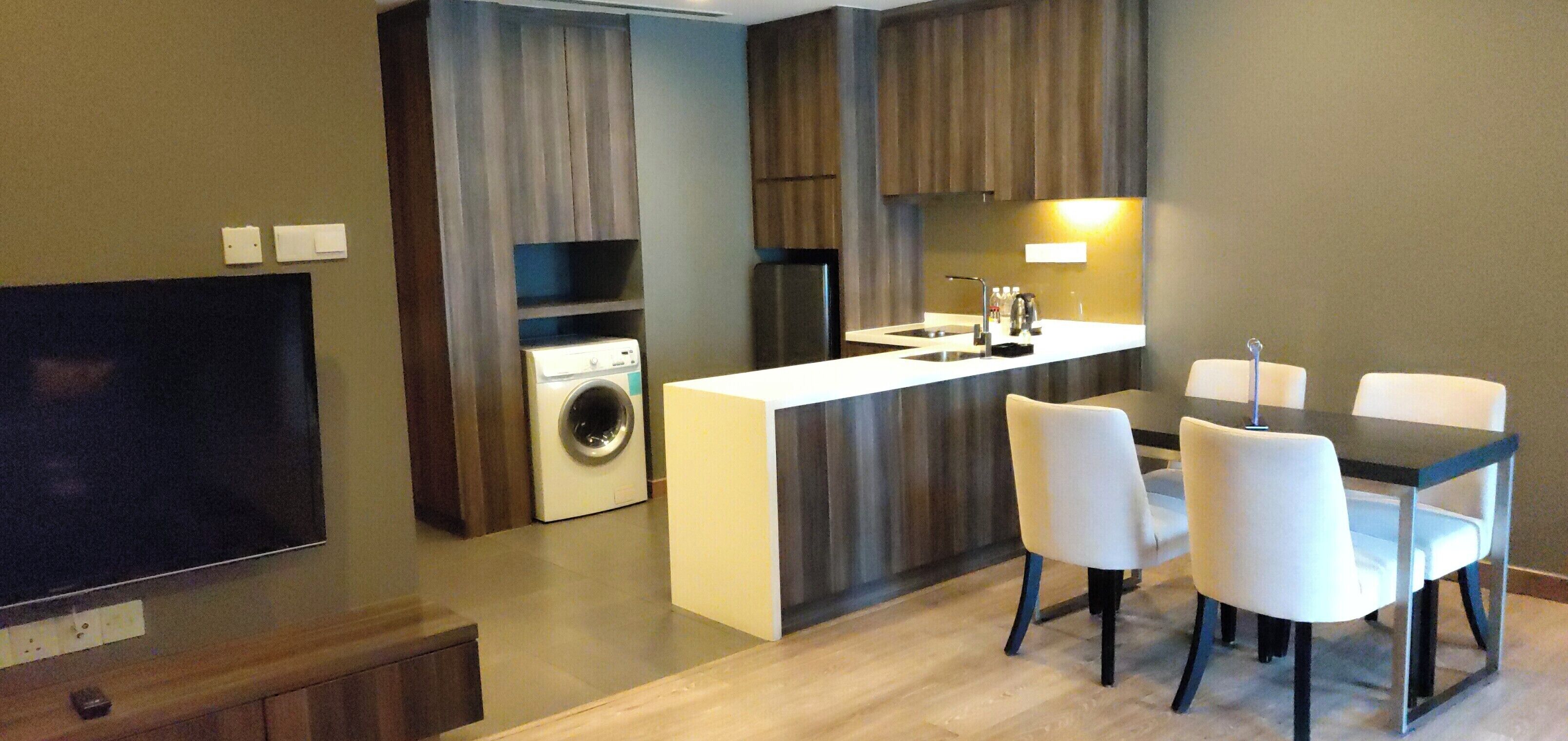 Una cocina compacta con lavadora y secadora integradas, una zona de comedor con mesa y sillas, y un televisor de pantalla plana montado en la pared.
