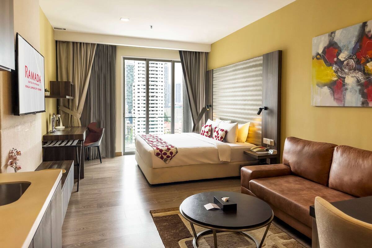 Une chambre d’hôtel comprenant un lit, un canapé, un bureau avec une chaise, une télévision et une grande fenêtre avec des rideaux.