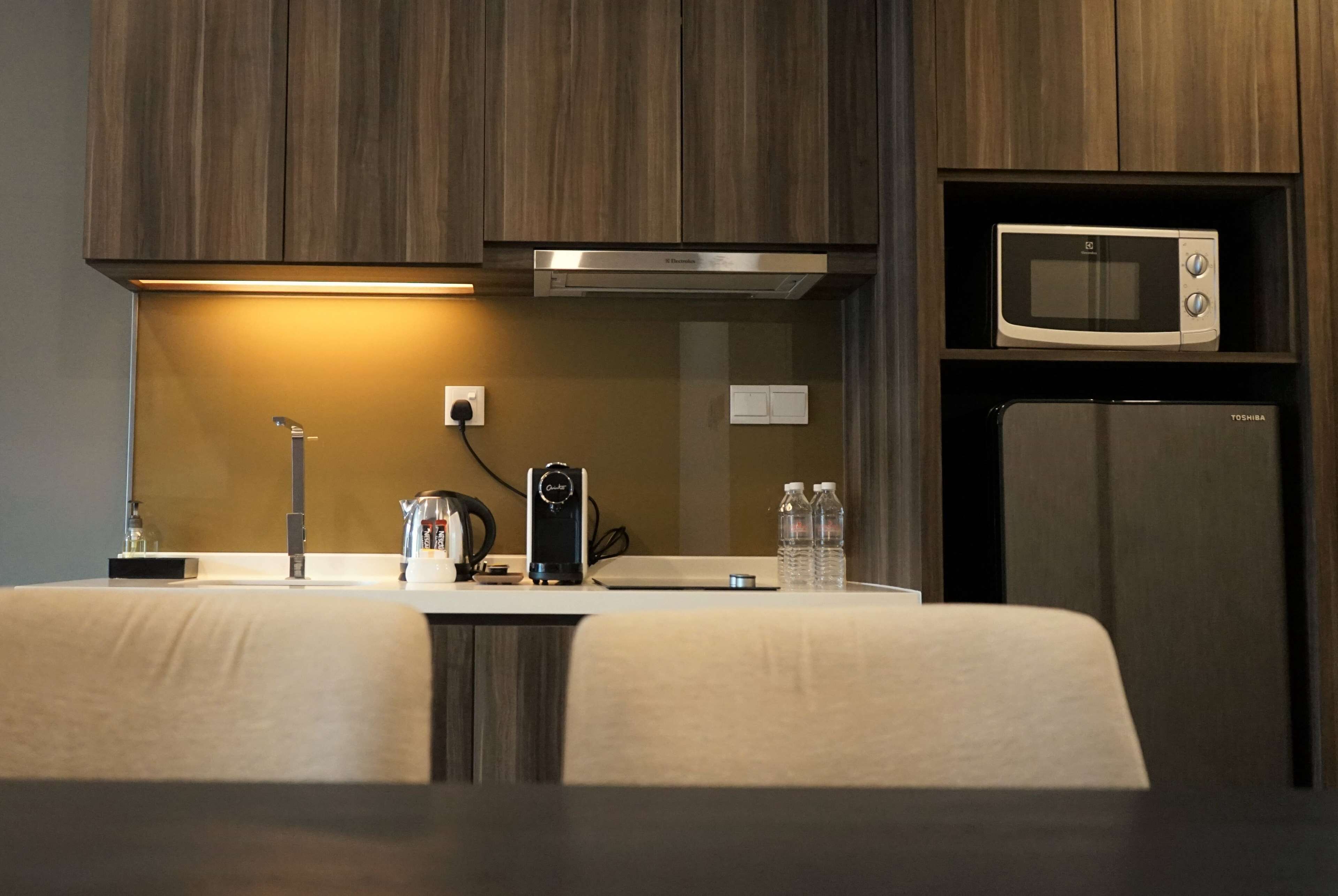 A modern kitchen with wooden cabinets, a built-in microwave, a coffee maker, and a water dispenser.