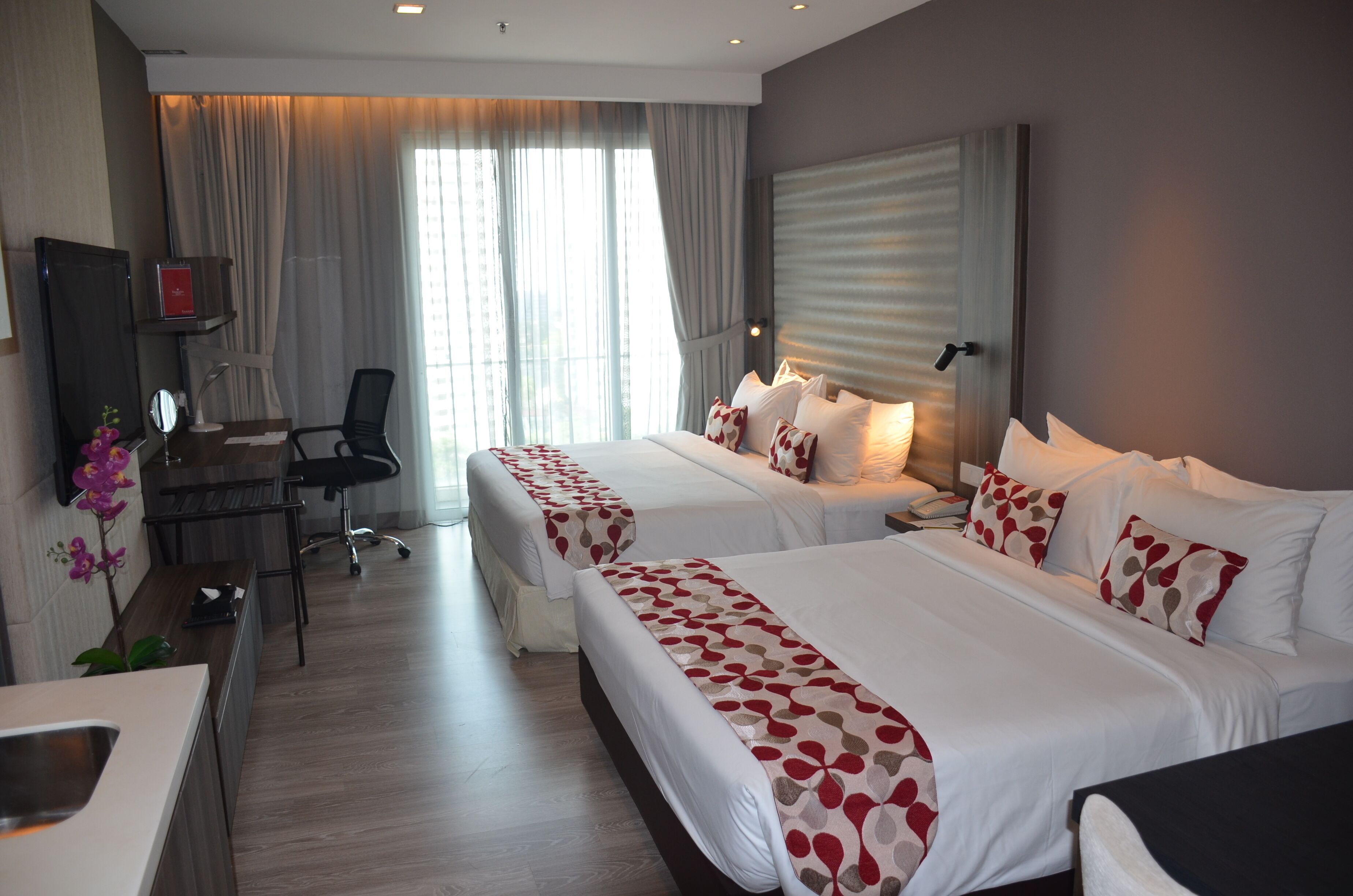 A hotel room with two beds, a desk with a chair, a TV, and a window with curtains.