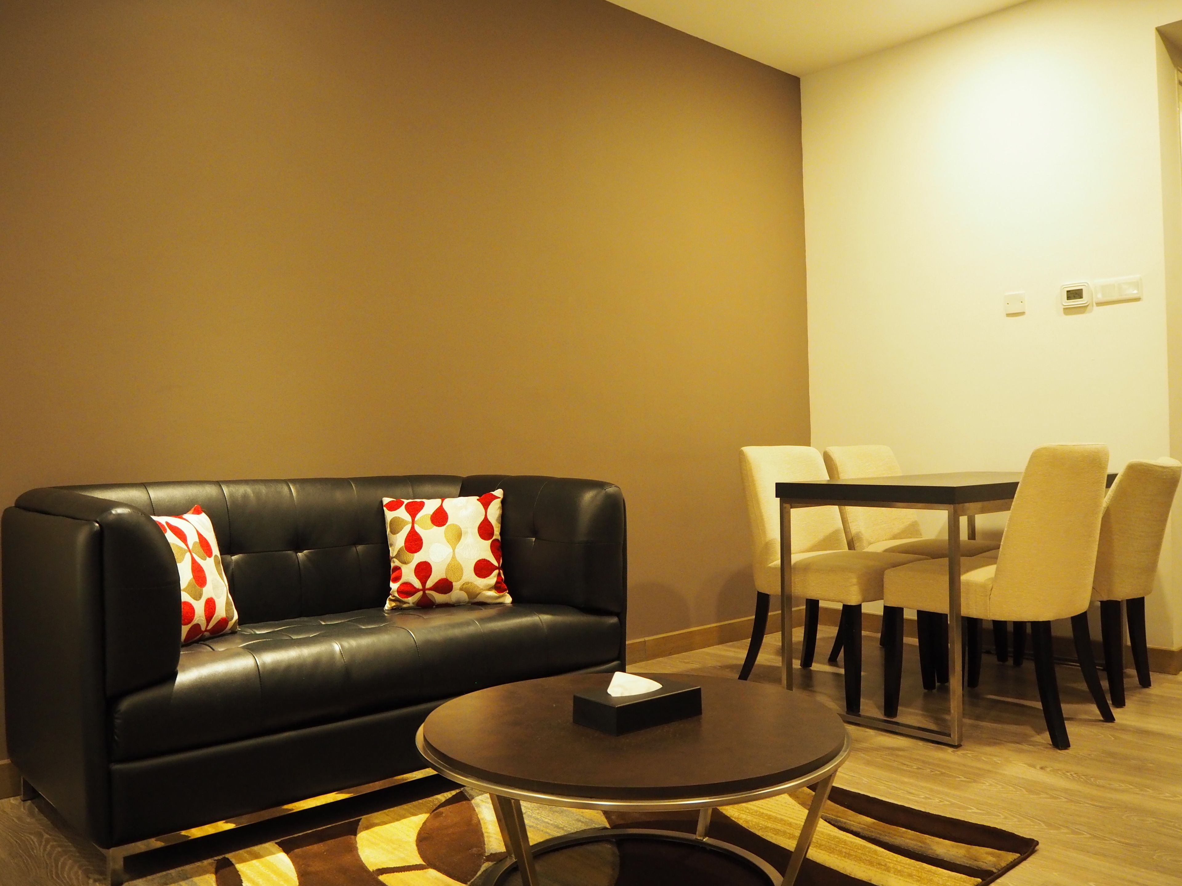 Un salon moderne avec un canapé en cuir noir, une table basse ronde et un coin repas comprenant une table et des chaises.