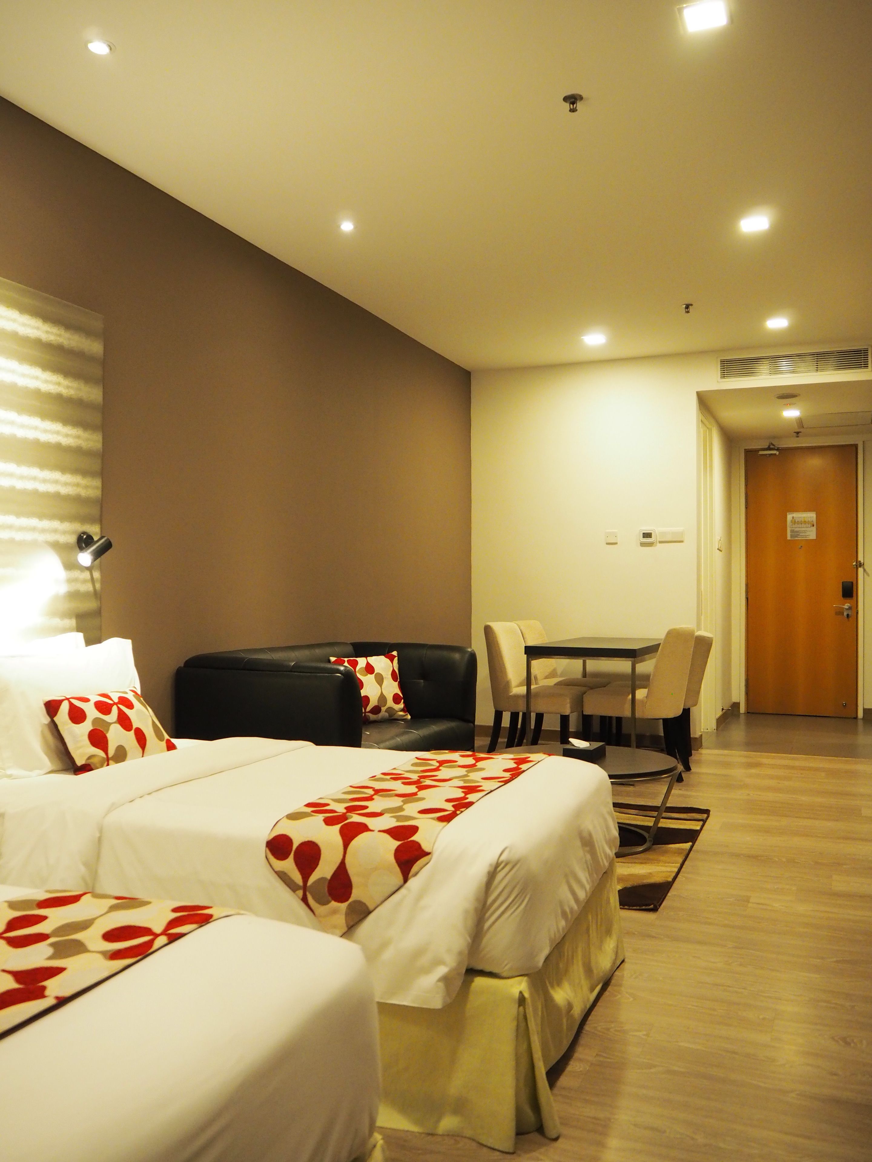 A hotel room with two beds, a sofa, a dining table, and a wooden floor.