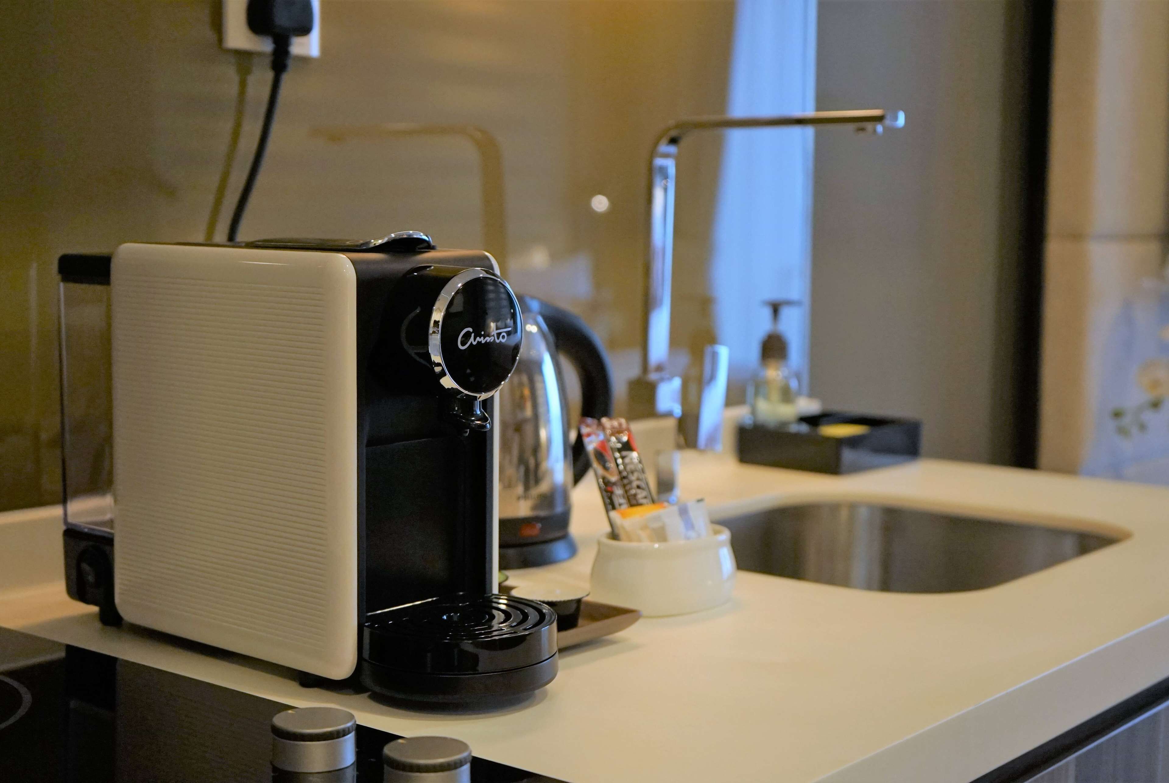 Una cafetera sobre la encimera de la cocina, con un lavabo y un soporte para cápsulas de café.