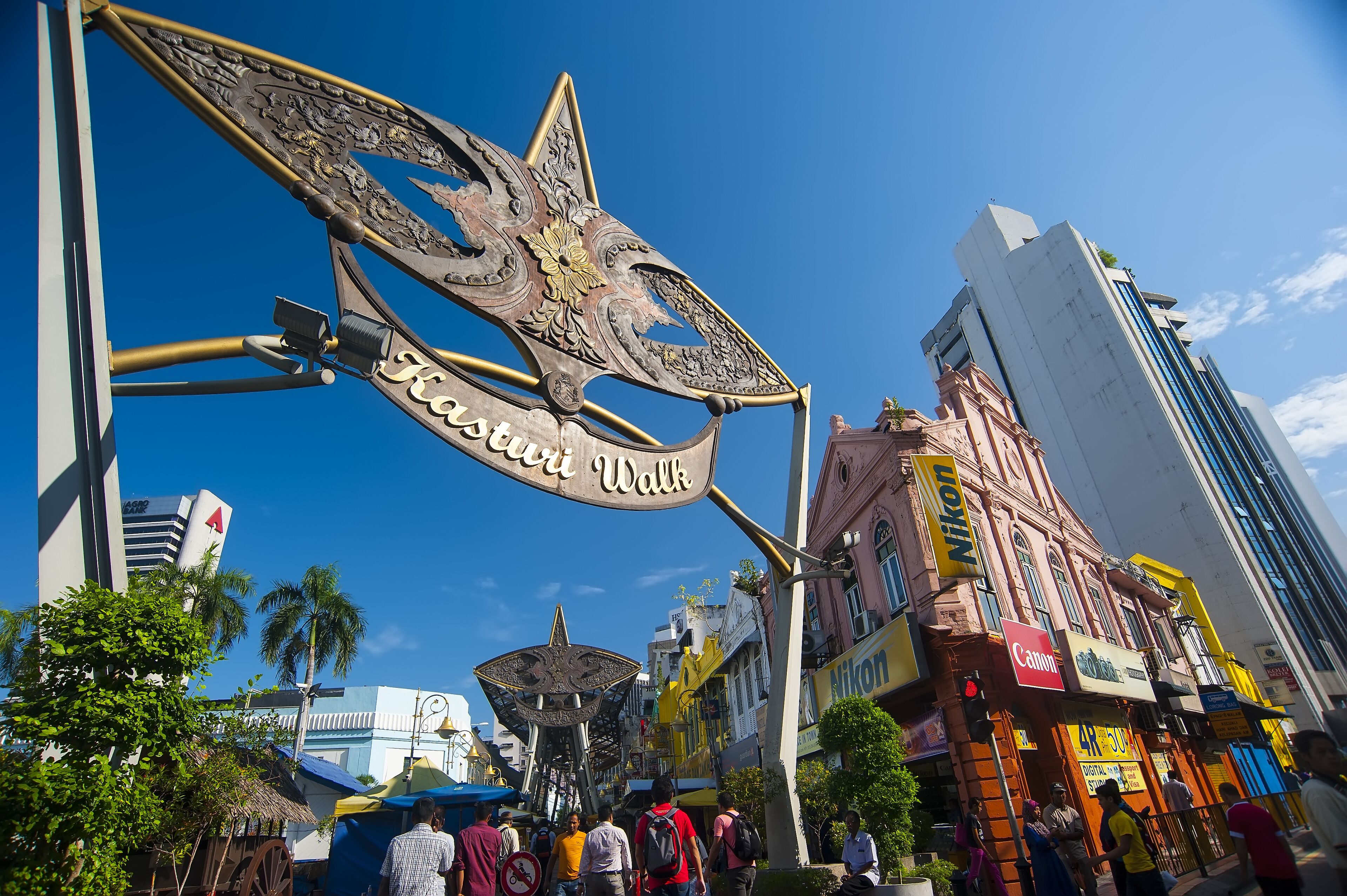 A street sign with 'Kasturi Walk' and a large decorative metal structure.