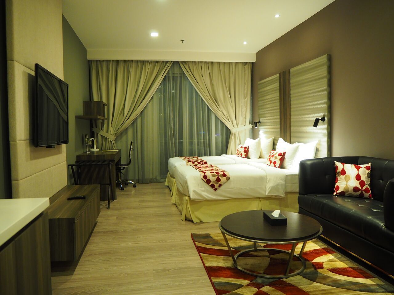 A hotel room with a bed, a sofa, a coffee table, a desk, and a TV.