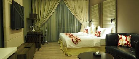 A hotel room with a bed, a sofa, a coffee table, a desk, and a TV.