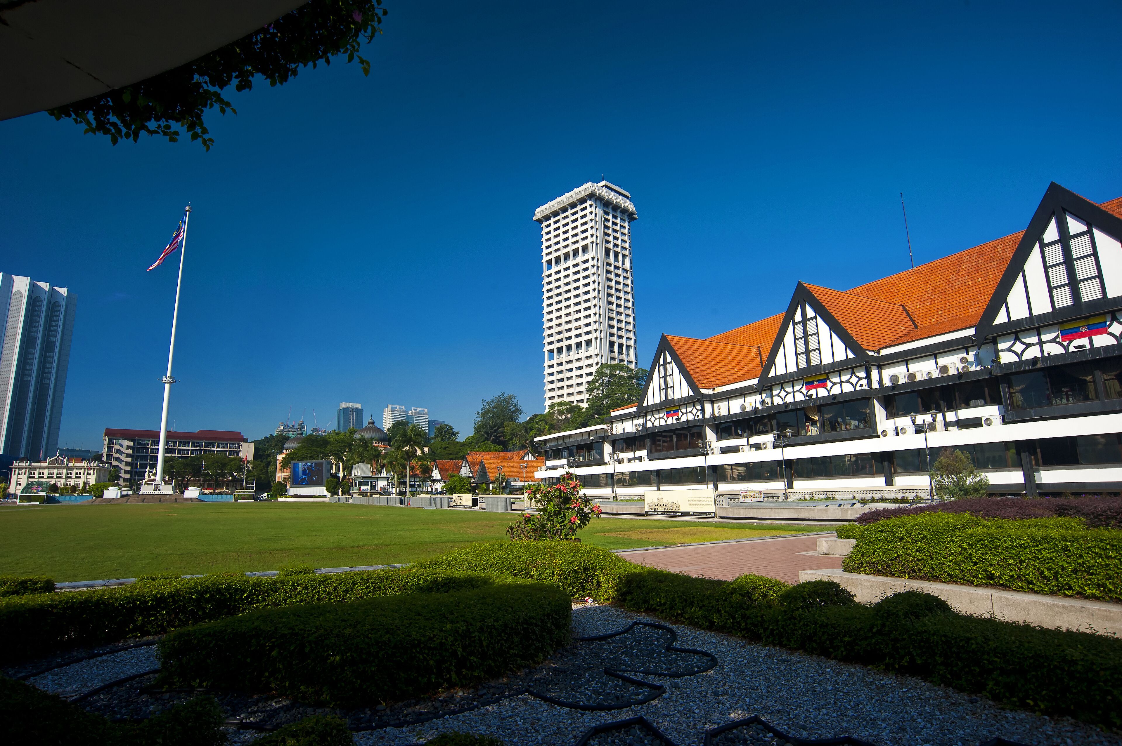 A cityscape with a tall building, a flagpole with a flag, and a traditional building with a red roof.
