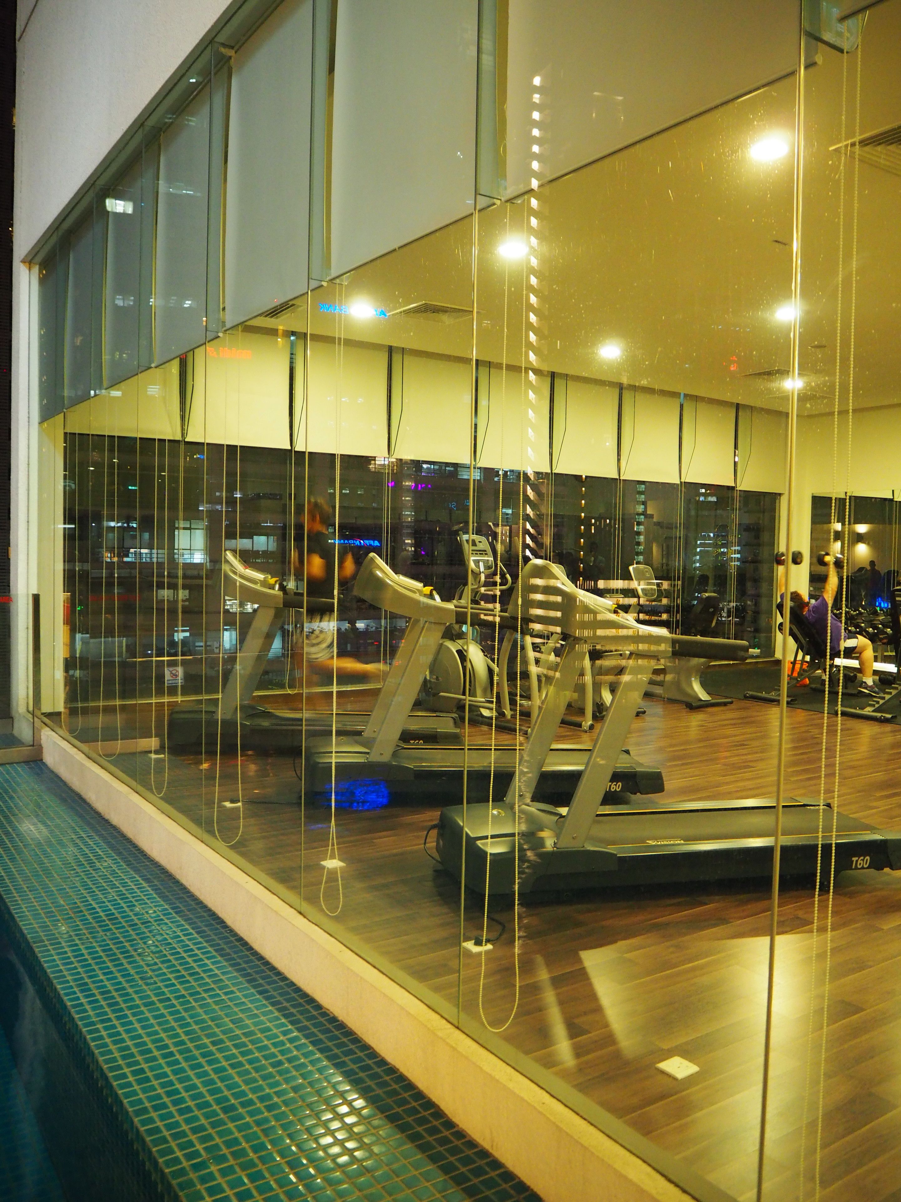 Ein Fitnessstudio mit Trainingsgeräten, großen Fenstern und gefliestem Boden.