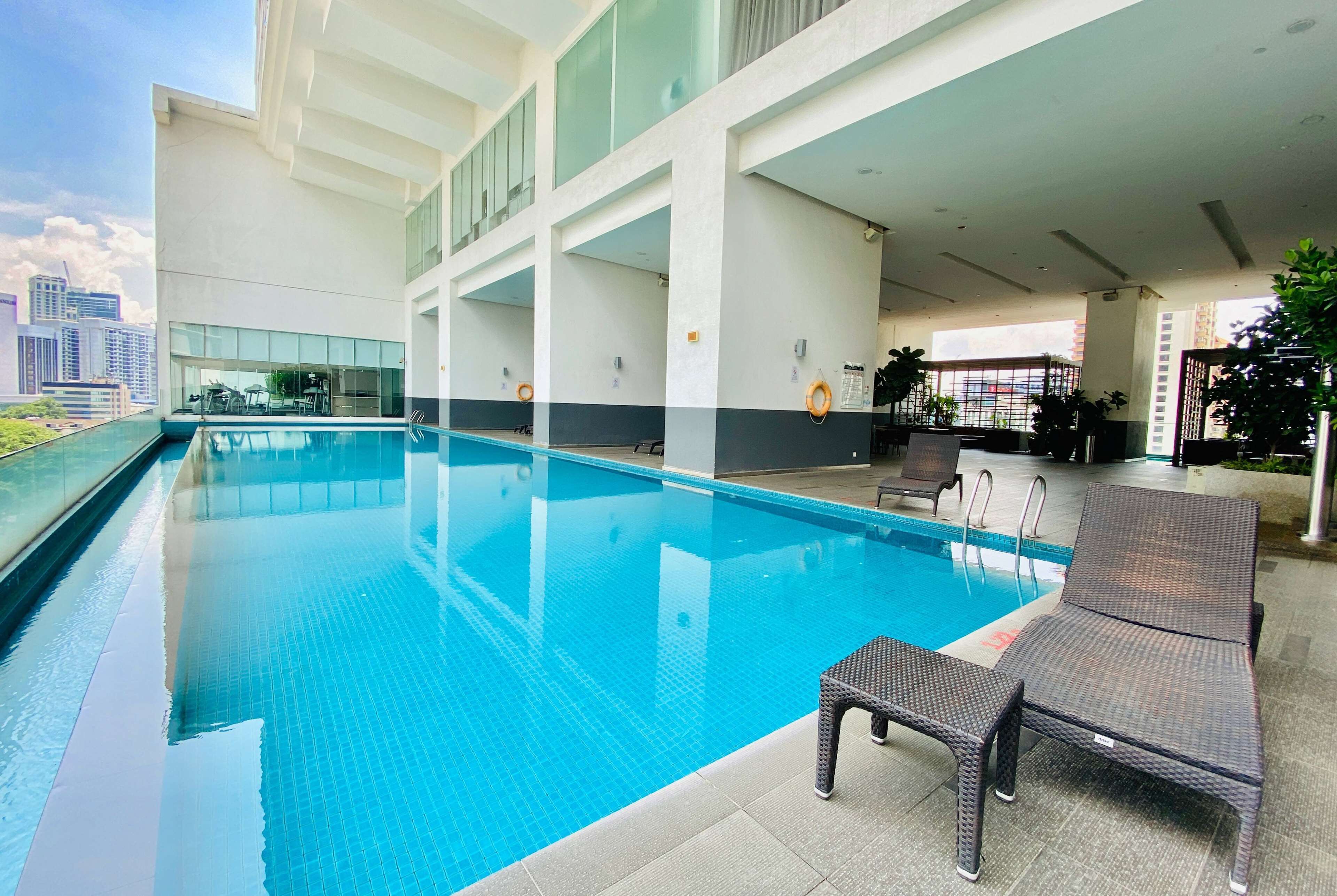 A modern indoor swimming pool with clear blue water, surrounded by lounge chairs and a city view.