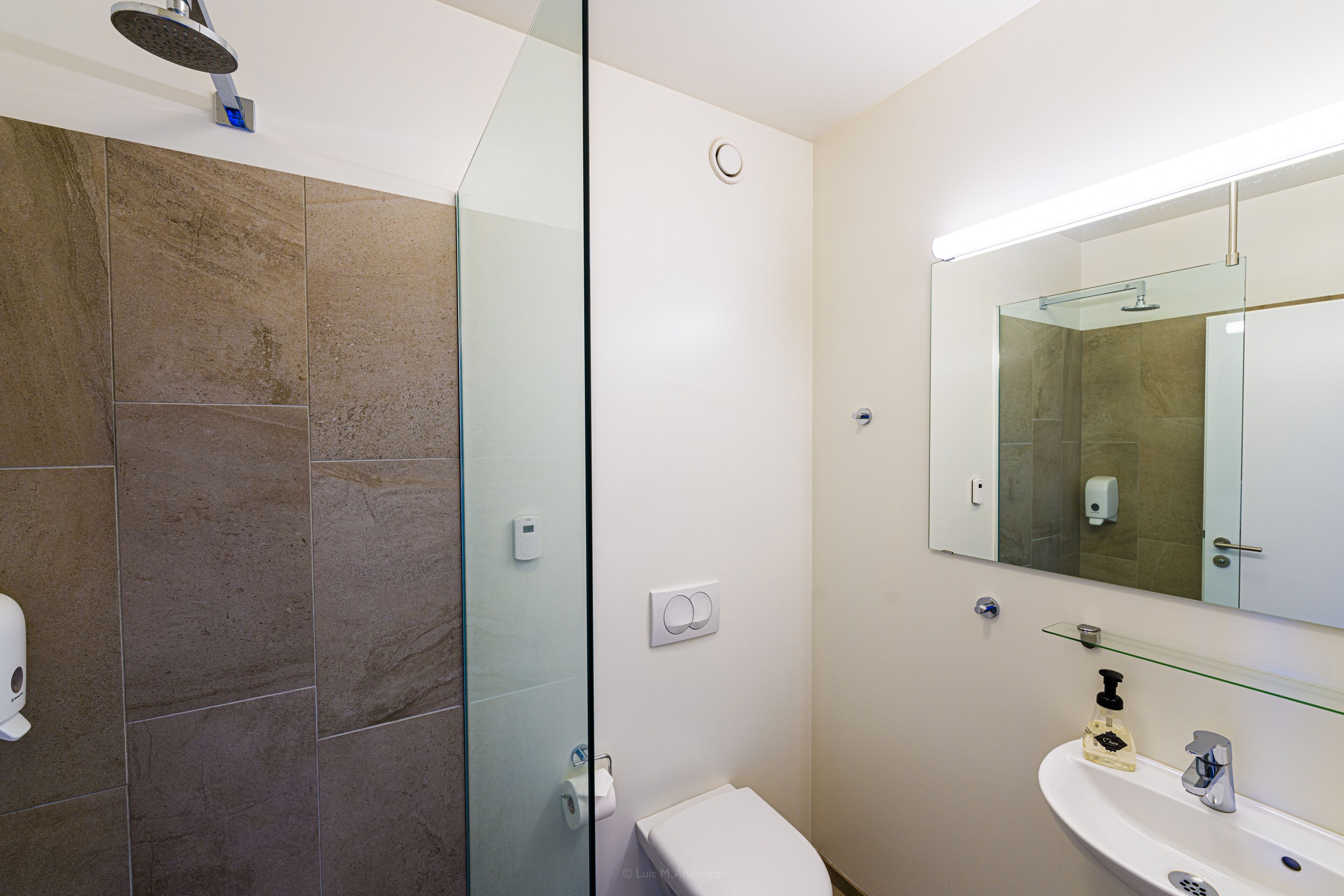 A modern bathroom with a glass shower enclosure, a white toilet, and a sink with a mirror above it.