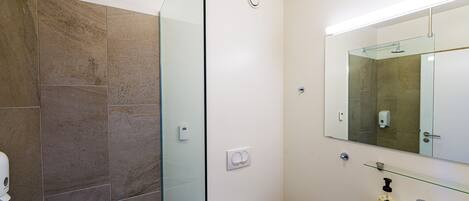 Un baño moderno con cabina de ducha de vidrio, inodoro blanco y lavabo con espejo sobre él.