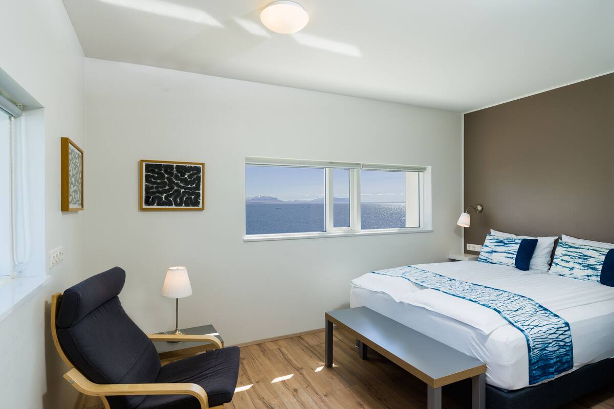 Une chambre d’hôtel moderne avec un grand lit, un bureau, une chaise et une fenêtre donnant sur un beau paysage.