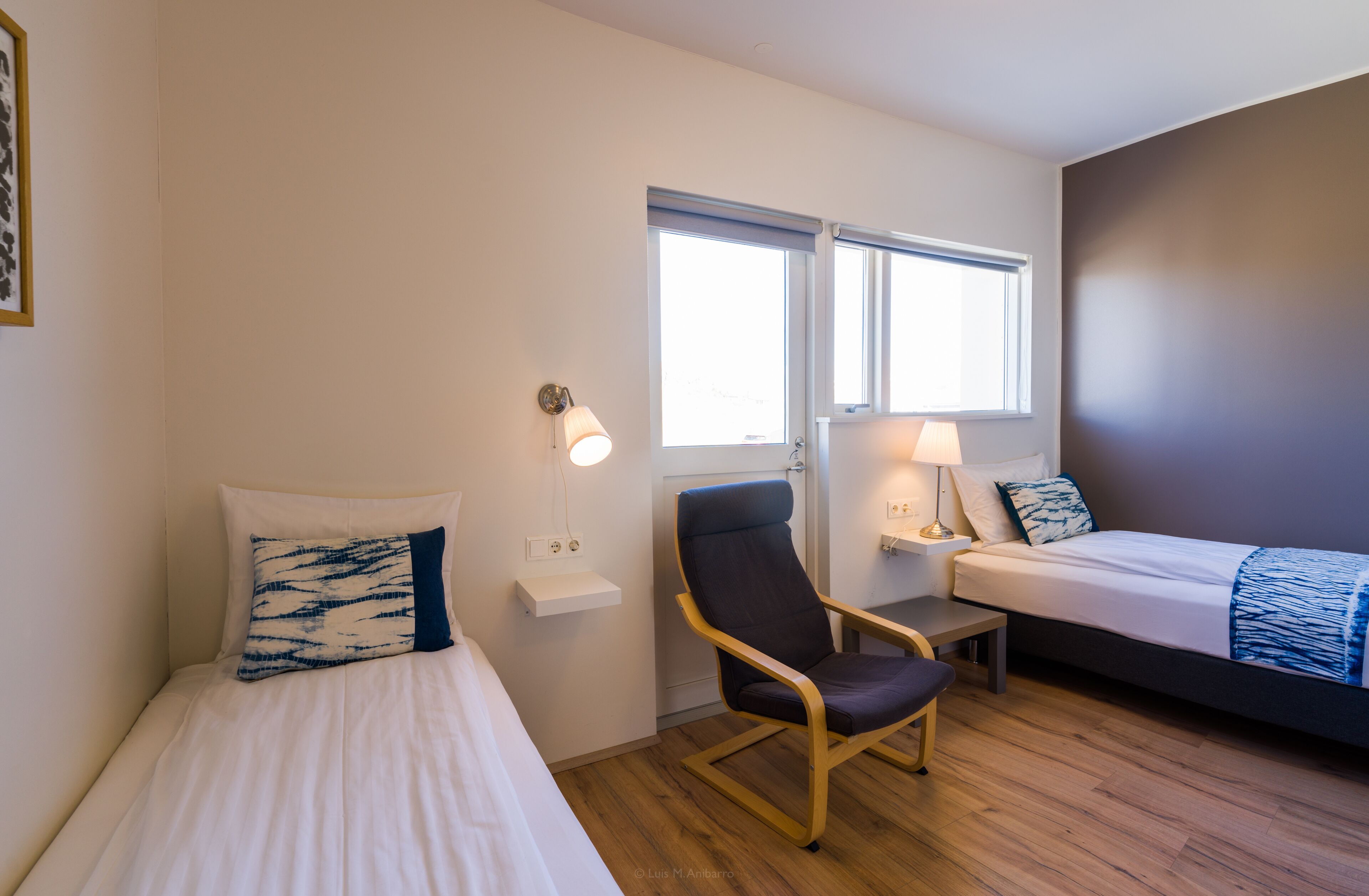 A hotel room with two beds, a chair, a nightstand, and a window.