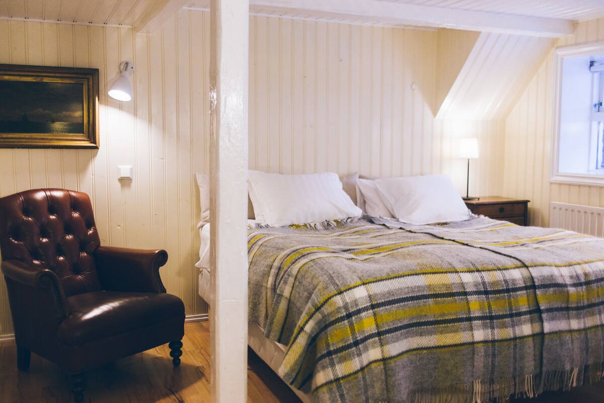 A bedroom with a bed, a chair, a nightstand, a lamp, and a window.