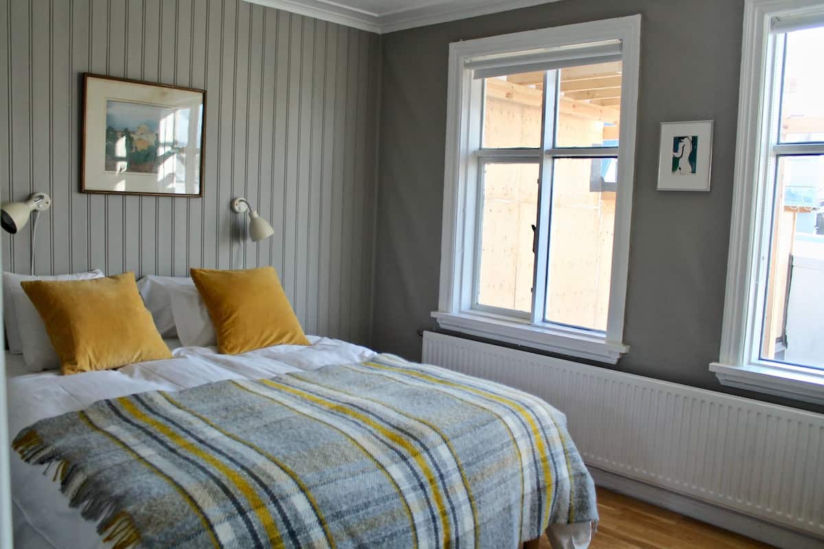 A bedroom with a bed, two bedside lamps, a window, and a radiator.
