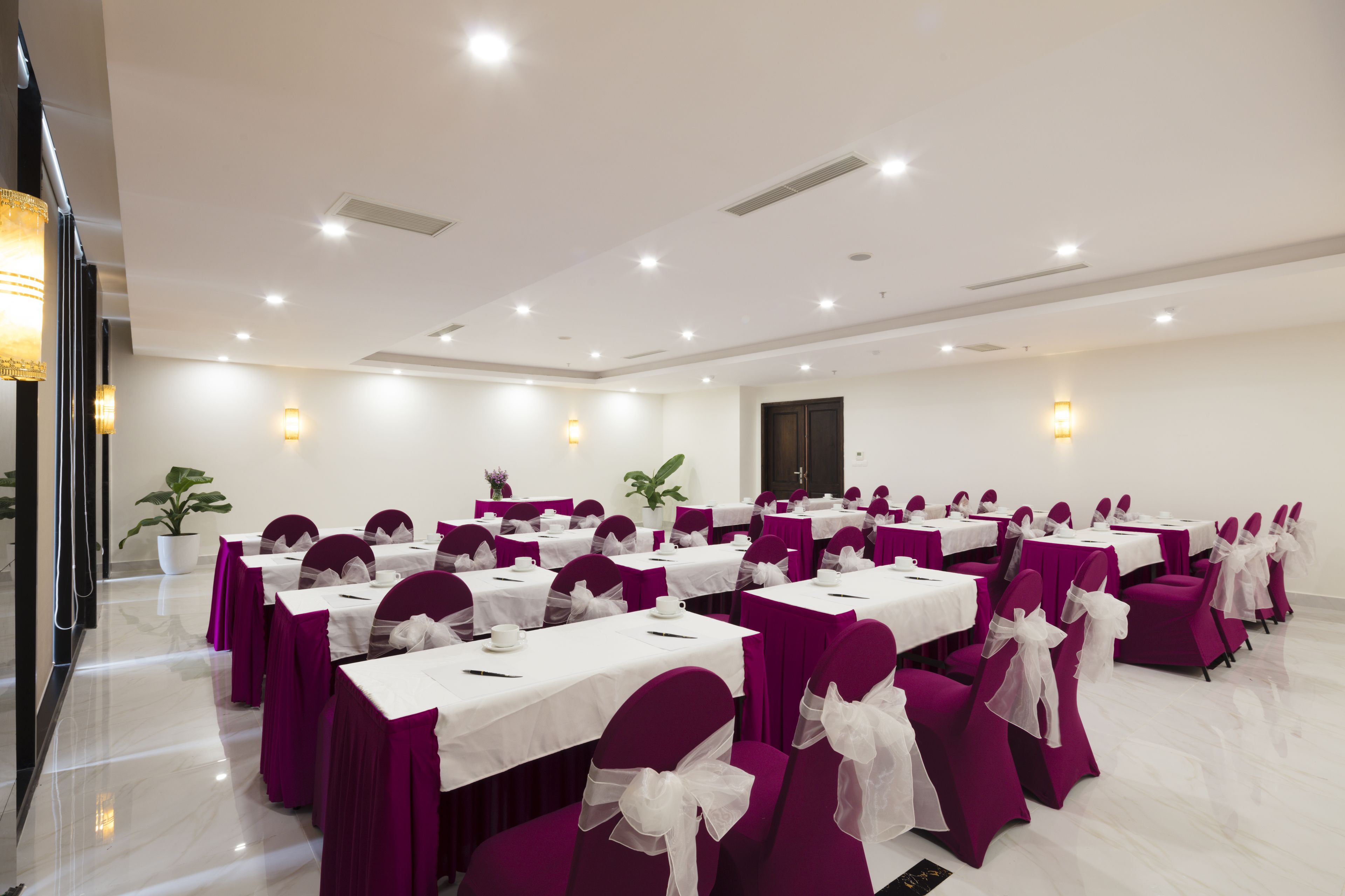 A conference room with rows of tables and chairs, each with a white tablecloth and purple chair covers.