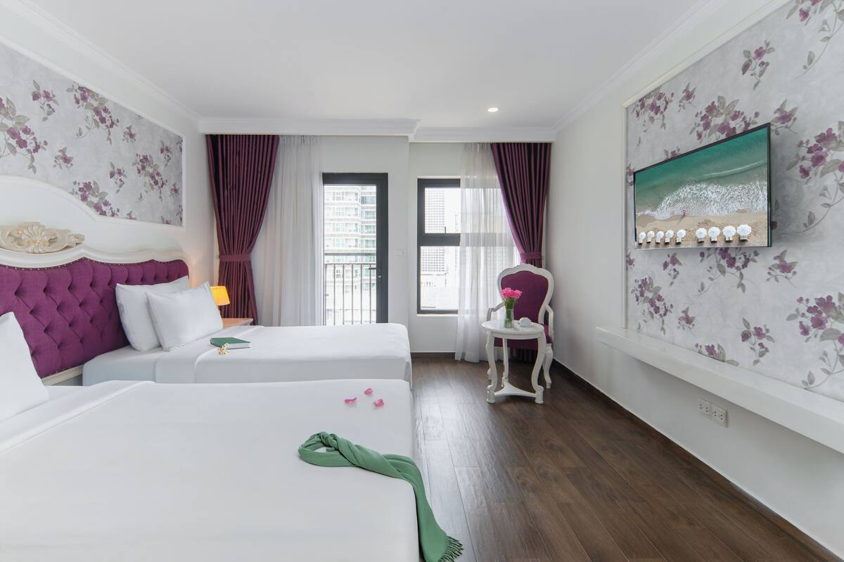 A hotel room with two beds, a vanity with a mirror, a small table, and a window with curtains.