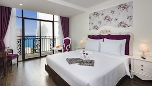 A hotel room with a large bed, a nightstand, a chair, and a view of the sea through a balcony. - Bonjour Nha Trang Hotel (Nha Trang)