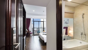 A hotel room with a balcony, a large bed, a bathroom with a bathtub, and a view of the city. - Bonjour Nha Trang Hotel (Nha Trang)
