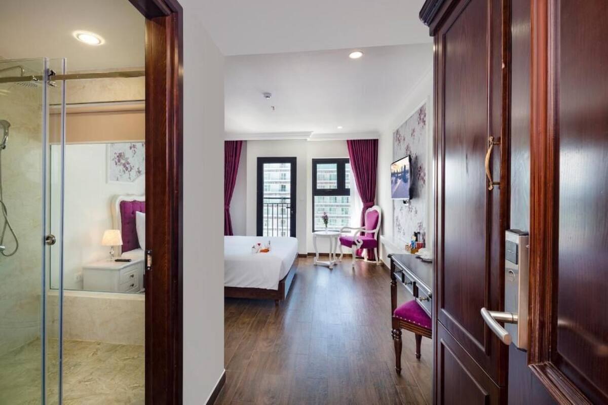 A hotel room with a glass shower, a bed, a desk, a chair, and a TV.