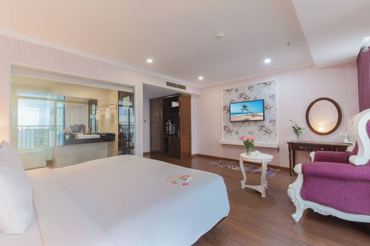 A hotel room with a large bed, a desk with a chair, a television, and a bathroom visible through an open door.